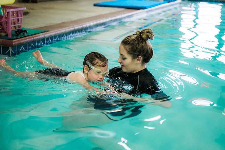 An adult student receiving personalized feedback from a swim instructor during a private session in a heated indoor pool.