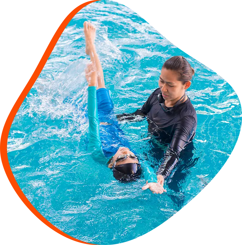 Adult swimmer practicing freestyle with a FINS instructor in a heated indoor pool at FINS Grand Parkway.