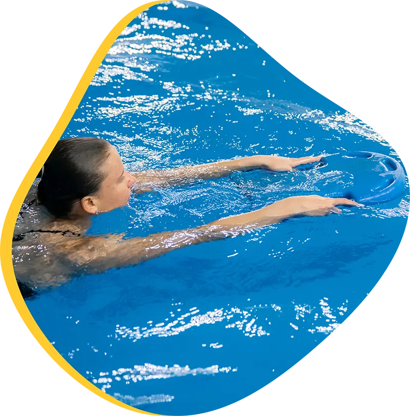 Adult swimmer practicing freestyle with a FINS instructor in a heated indoor pool at FINS Grand Parkway.