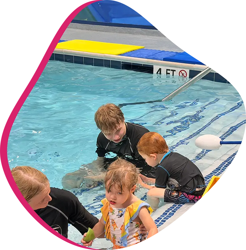 Parent assisting baby during infant swim lesson at FINS Swim School—The Woodlands indoor pool.