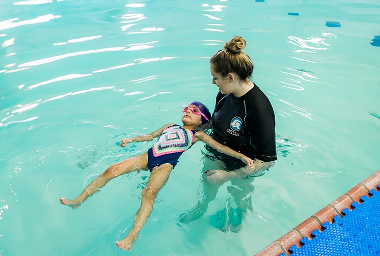 An adult student receiving personalized feedback from a swim instructor during a private session in a heated indoor pool.